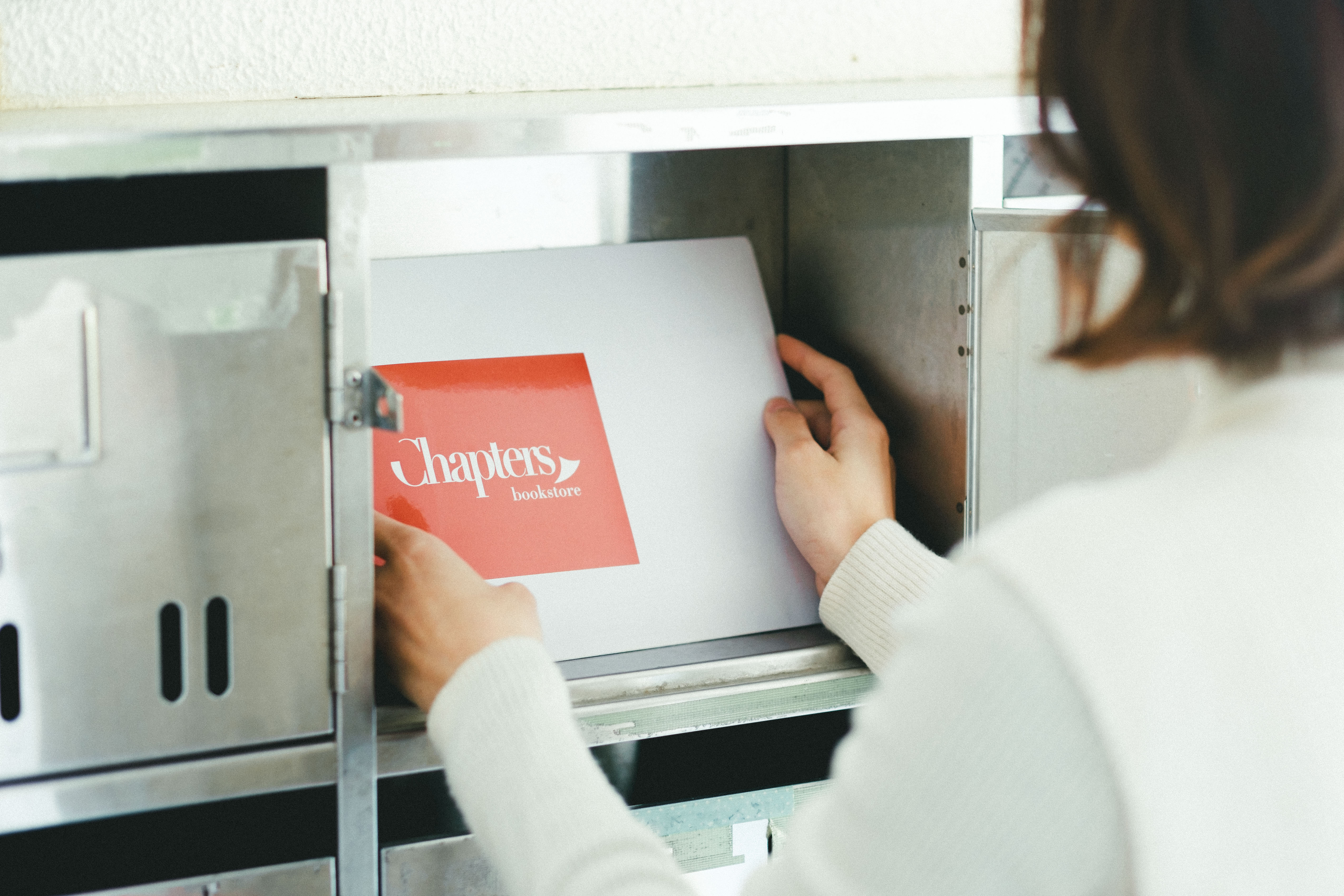 集合ポストの扉を開け、チャプターズのロゴが入った封筒を受け取る女性の手元