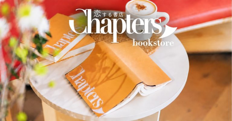 「恋する書店 Chapters bookstore」のロゴと、山吹色のオリジナルカバーをかけた文庫本、カフェラテが白い丸テーブルに置かれた写真